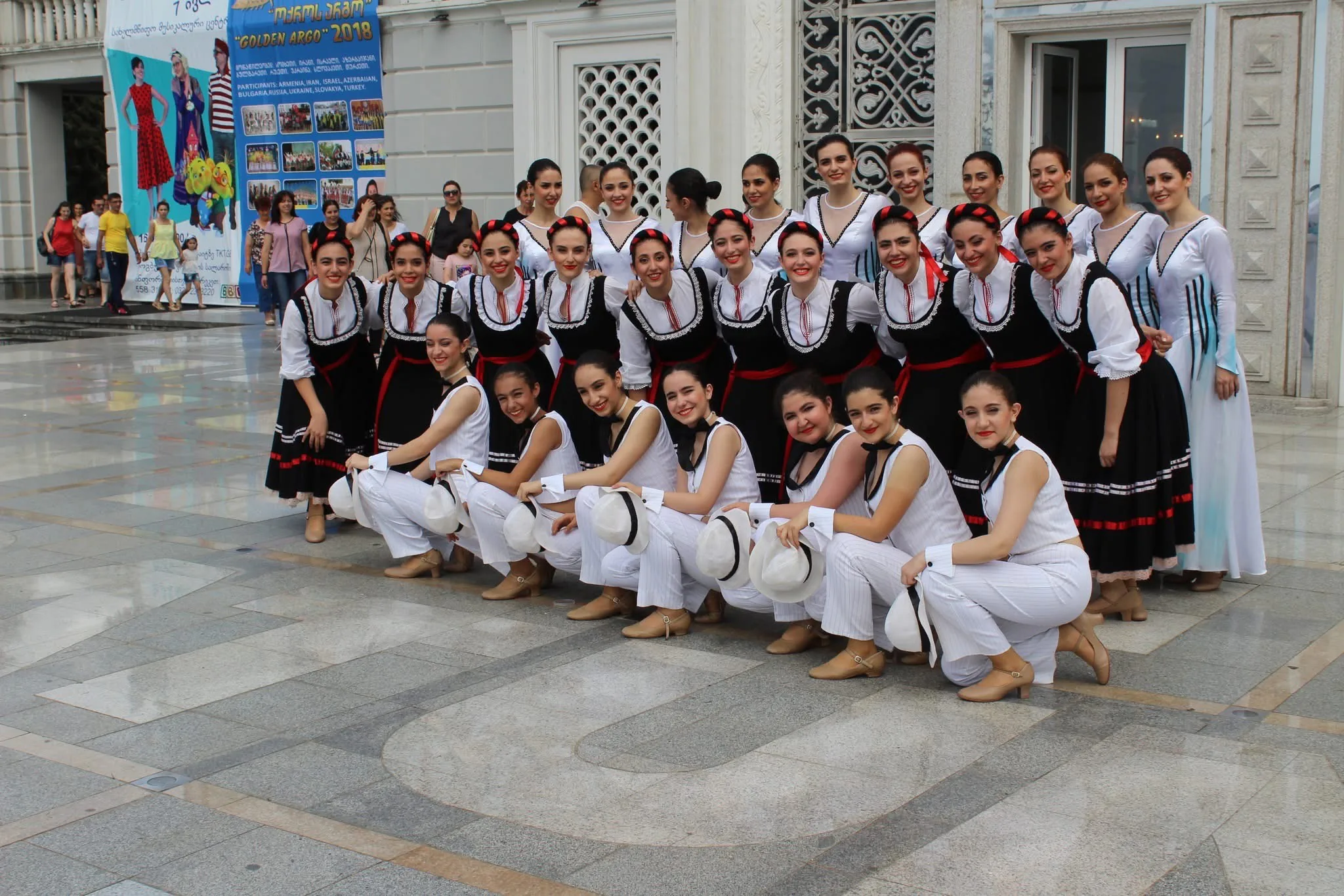 A large folk-dance ensemble gathered outside in traditional dress