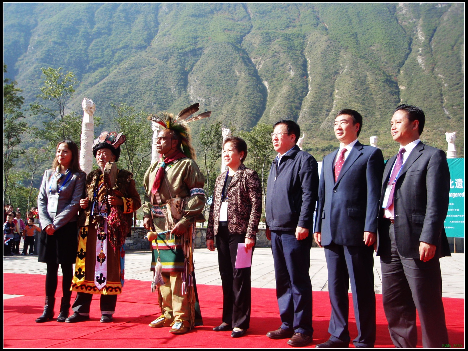 Seven participants standing outdoors before mountain slopes at a cultural-protection forum in Jiuzhaigou