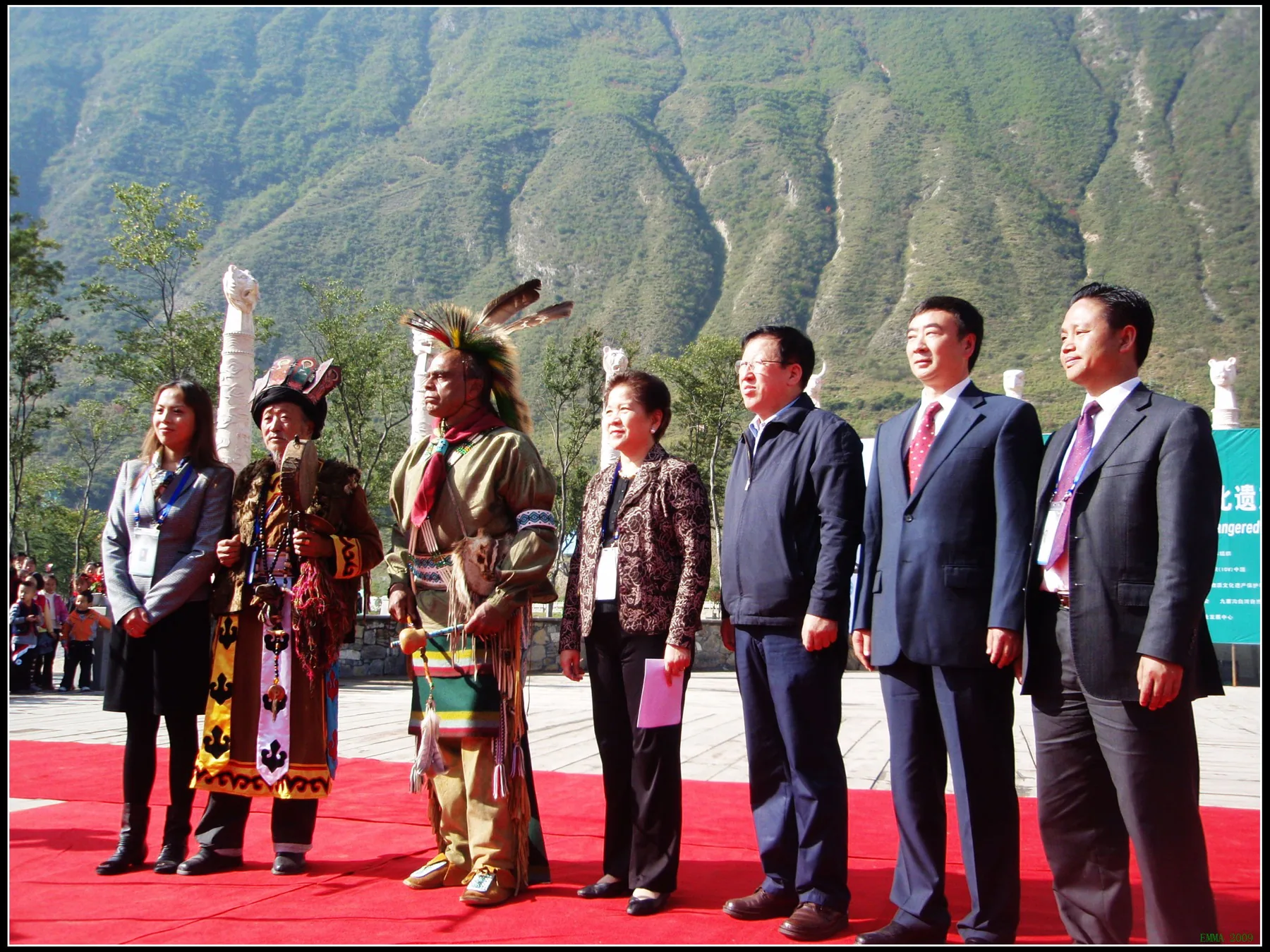 Seven participants standing outdoors before mountain slopes at a cultural-protection forum in Jiuzhaigou